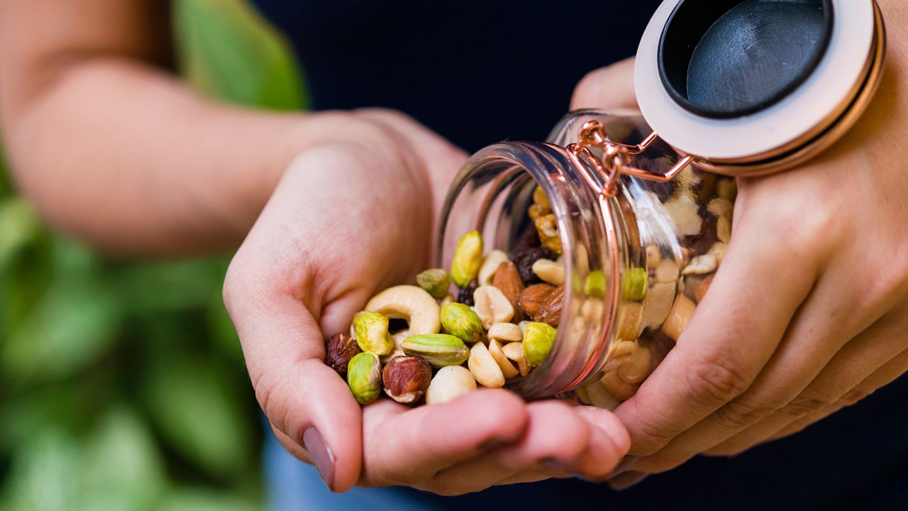 Mano de modelo morena sosteniendo un bote de vidrio hermético con una mezcla de nueces.
