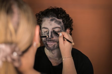 Un maquillador pinta la cara de un joven