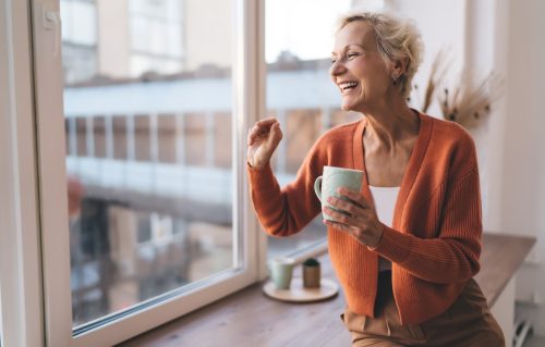Una mujer mayor con estilo se ríe con una rebeca naranja y una taza de café