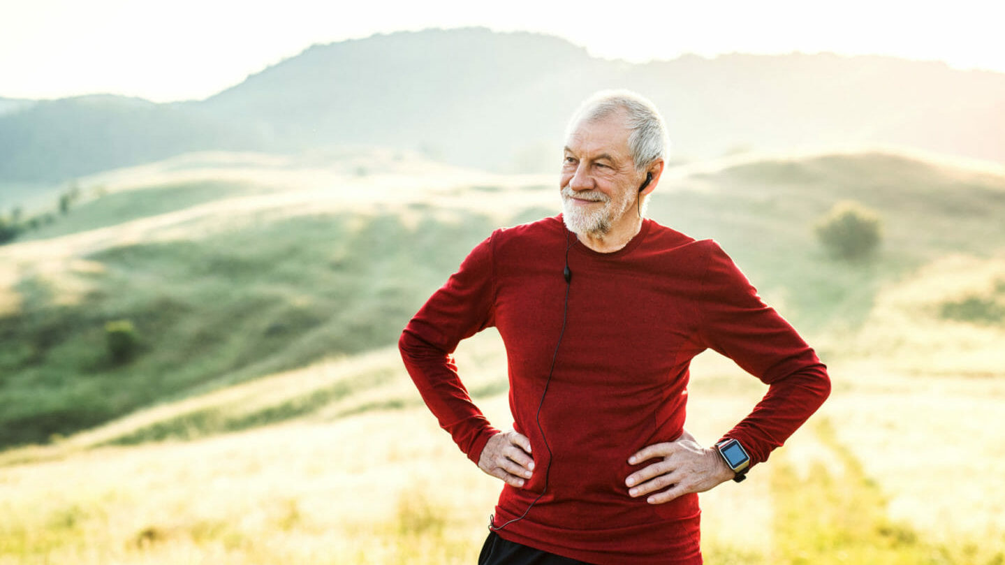 A senior man resting during exercise, taking in a view of hills.