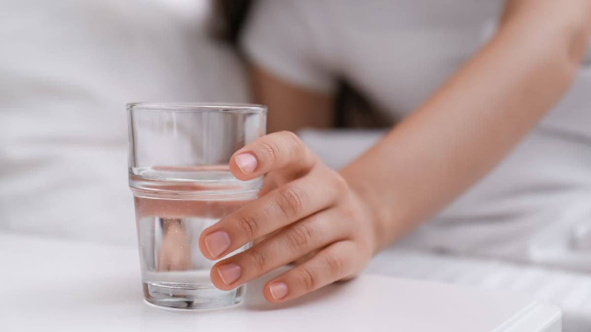 Una mujer toma un vaso de agua junto a la cama.