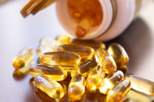 Cápsulas de aceite de pescado con omega 3 y vitamina D en una botella de vidrio sobre una textura de madera, concepto de nutrición, primer plano.