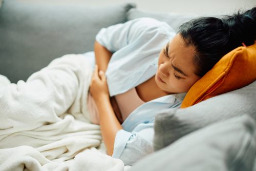 Mujer joven acostada en la cama sosteniendo el estómago con síntomas de intoxicación alimentaria o dolor de estómago
