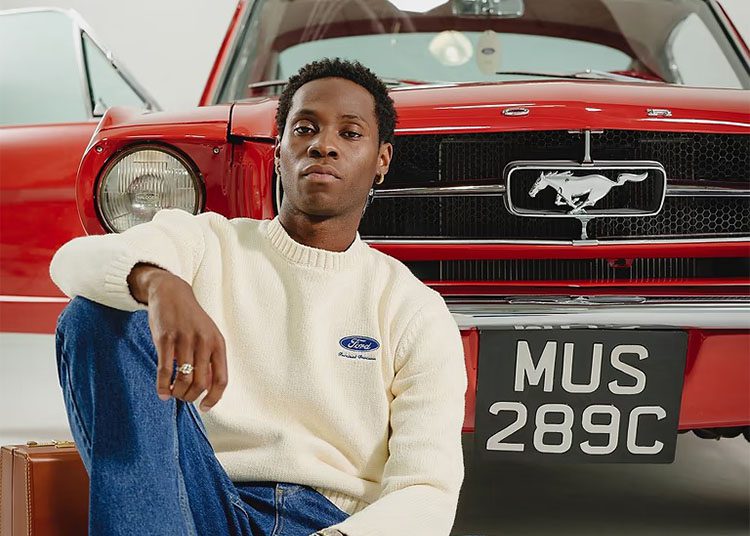 Un hombre que vive una vida de lujo se sienta frente a un viejo Ford Mustang rojo, leyendo sus matrículas. 