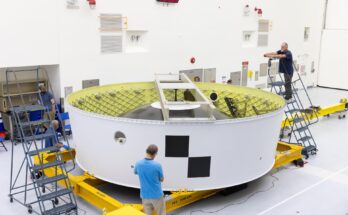 Image shows a white and yellow cylinder piece of hardware with technicians inspecting and taking photos of the Orion stage adapter at NASA's Kennedy Space Center in Florida. Photo credit: NASA/Kim Shiflett