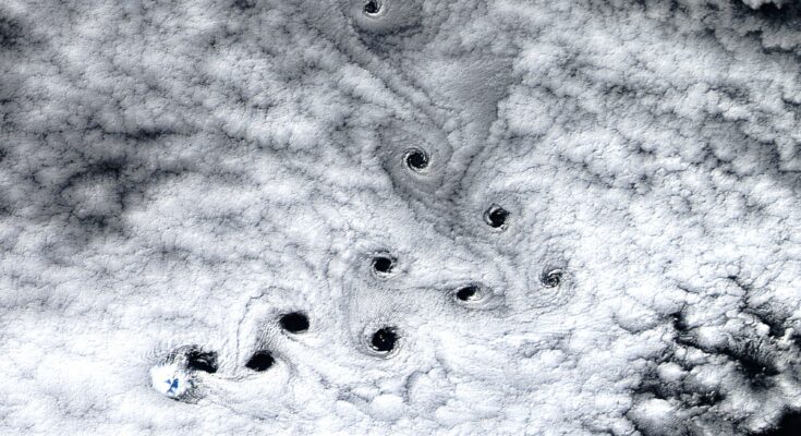 A satellite photo sowing ten dark holes in the clouds swirling in the sky