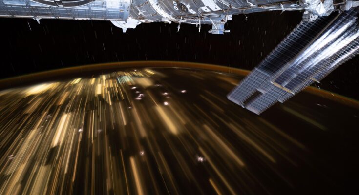 The warm city lights of Southeast Asia streak below the silvery U.S. segment of the International Space Station in this 30-second exposure from the orbital outpost as it soared 259 miles above China at approximately 10:39 a.m. local time. Near the top center, is the partially obscured SpaceX Dragon spacecraft that docked to the Harmony module's forward port carrying NASA's Crew-11 mission.