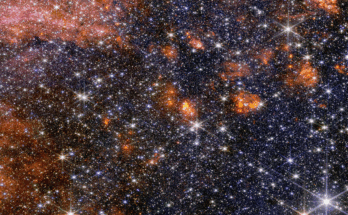 A wide view of a region of space filled with stars and clumps of orange clouds.