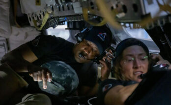A man and a woman hunch over in a small capsule, both looking at separate electronic screens