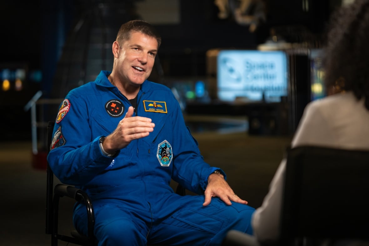 Un hombre azul de Bootsonaut, levantando su mano derecha mientras habla con la periódica.