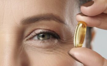 A person holding a vitamin near their blue-green eye.