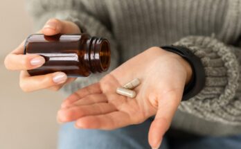 A person pouring beige capsules into their hand while wearing a grey knit sweater.
