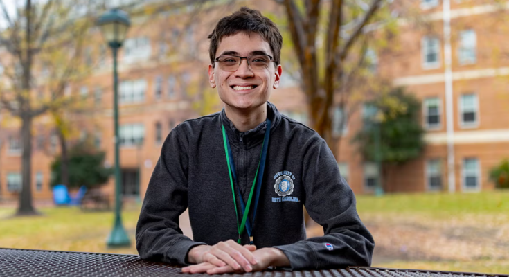 Daniel Meng-Saccoccio sits outside at a table smiling at the camera.