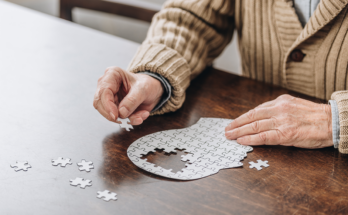 Cropped view of an elderly individual working on a puzzle shaped like a human head.