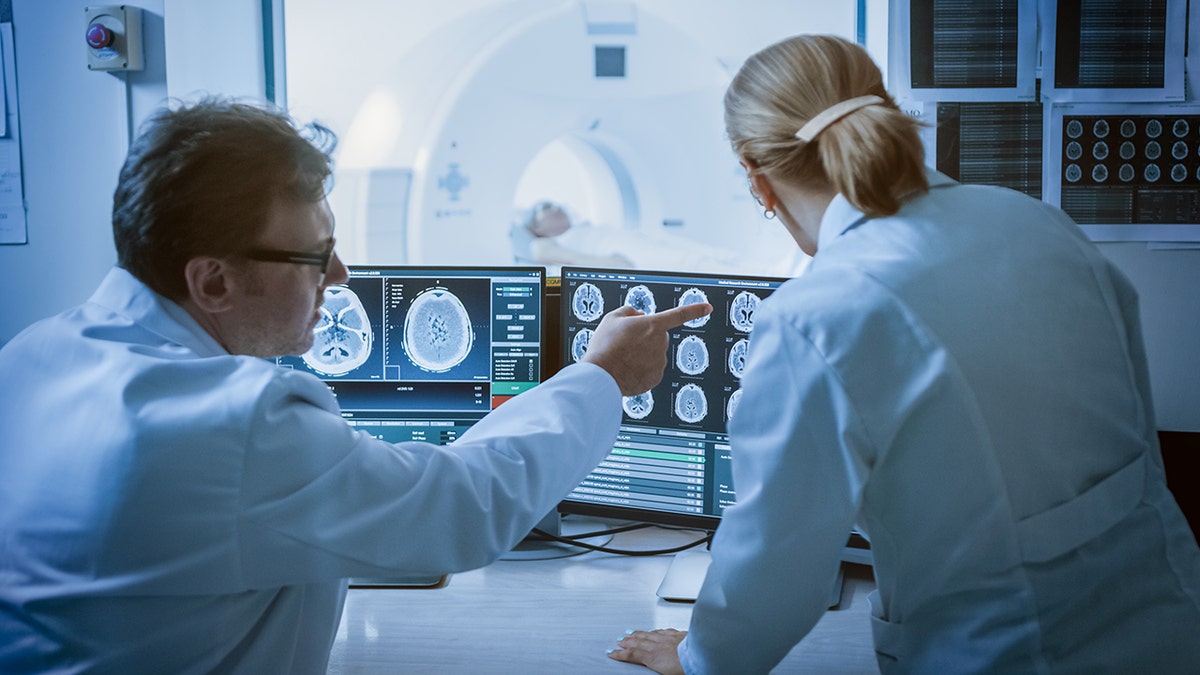 Los médicos que realizan resonancias magnéticas cerebrales examinan los monitores de computadora en la sala de control de radiología de un hospital.