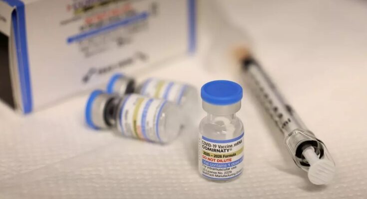 Close-up of a COVID-19 vaccine vial labeled Comirnaty beside a syringe, with additional vials and packaging blurred in the background. Photo from LA Times article not for re-use.